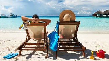 Symbolbild: Ein Pärchen in Liegestühlen am Strand und schaut auf türkisblaues Meer. In Griechenland werden Strandliegen nun beschränkt.  | Bild: BR-Bil/Adobe/Haveseen