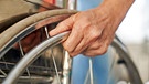 Hand eines Patienten am Reifen eines Rollstuhls als Symbol für Behinderung und Paraplegie | Bild: picture alliance / Zoonar | Robert Kneschke