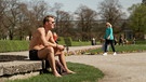 Mann mit nacktem Oberkörper und kurzen hosen sitzt in einem Park | Bild: BR