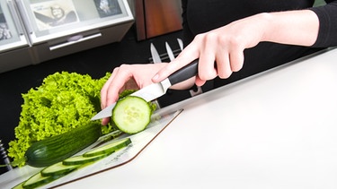 Eine Frau schneidet in einer Küche eine Salatgurke in Scheiben. | Bild: picture-alliance/dpa