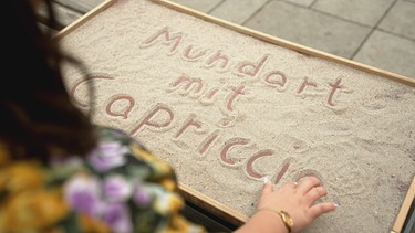 Der Shriftzug "Mundart mit Capriccio" mit den Findern in den Sand geschrieben. | Bild: BR