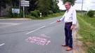 Ein Mann zeigt auf eine Schrift auf dem Straßenbelag. | Bild: BR