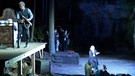 Ein Schauspieler steht auf der Bühne mit einem Gewehr in der Hand (links), während eine Frau vor der Bühne sitzt und das Stück in Gebärdensprache übersetzt | Bild: BR