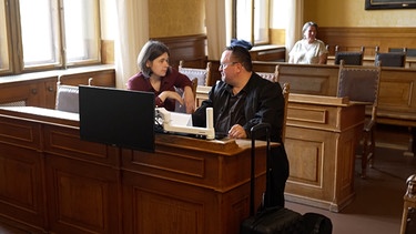 Die Klägerin, die Impfschäden durch den AstraZeneca Impfstoff erlitten hat, sitzt hier vor Gericht mit ihrem Anwalt. | Bild: BR