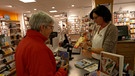 Die Verkäuferin in einem Buchladens scannt das Buch ihrer Kundin an der Kasse ein. | Bild: BR