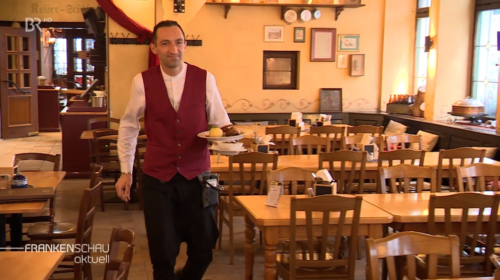 Ein Kellner trägt einen Teller mit Essen durch einen leeren Gastraum | Bild: BR Fernsehen
