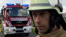 Alexey Shelbakh steht in Feuerwehr-Montur vor einem Einsatzfahrzeug. | Bild: BR