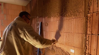 Ein Handwerker verputzt eine Wand mit einem Gemisch aus gemahlenen Haselnussschalen. | Bild: BR