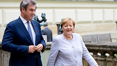 Markus Söder (CSU), Ministerpräsident von Bayern, begrüßt Angela Merkel (CDU), frühere Bundeskanzlerin, vor der Residenz in München. | Bild: picture alliance/dpa | Sven Hoppe