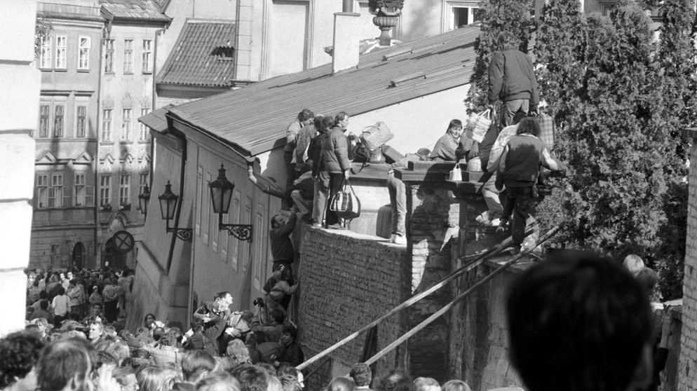 Ausreisewillige DDR-Bürger klettern im September 1989 über eine Mauer auf das Gelände der bundesdeutschen Botschaft in der tschechoslowakischen Hauptstadt Prag. | Bild: picture-alliance/dpa