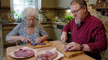 Lore Huber und ihr Sohn Uli schneiden verschiedene Fleischsorten für die Milzwurst auf. | Bild: BR/Daniel Delbeck