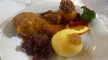 Gebratene Ente mit hausgemachten Kartoffelklößen, Rotkraut, glasierten Maronen und Bratapfel mit Marzipan-Zwetschgenfüllung | Bild: BR/Andi Christl