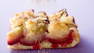 Ein Stück Zwetschgendatschi mit Streuseln steht auf einer weißen Tischplatte und wird mit Zucker bestreut. | Bild: mauritius images / foodcollection