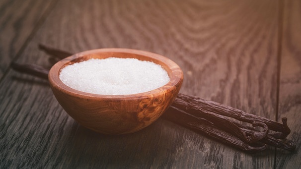 Ein Holzschälchen mit Zucker und vier Vanilleschoten daneben auf einem Holztisch | Bild: mauritius images / Vladislav Gudovskiy / Alamy