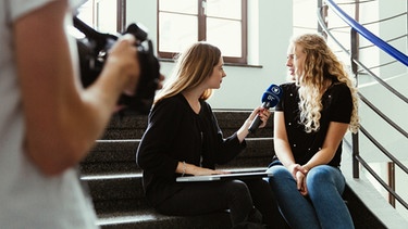 Eine junge Frau interviewt eine andere. Ein junger Mann filmt das Gespräch. | Bild: BR/Sylvia Bentele