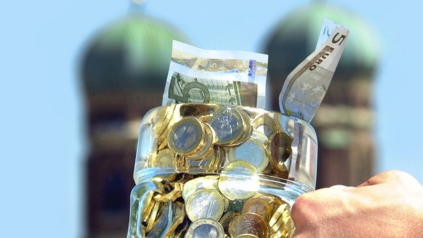 Einen Bierkrug voll Geld vor der Münchner Frauenkirche | Bild: picture-alliance/dpa