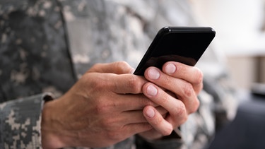 Soldat umfasst Handy mit beiden Händen | Bild: imago images
