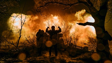 Soldat mit erhobenen Siegesfäusten, im Hintergrund flammendes Inferno | Bild: picture-alliance/dpa