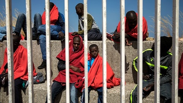 Migranten hinter Mauern/Gitterstäben in Decken gehüllt | Bild: picture-alliance/dpa