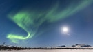 Nordlicht (Aurora Borealis) bei Vollmond über verschneiten Bergen in Lappland (Schweden). | Bild: picture alliance/imageBROKER