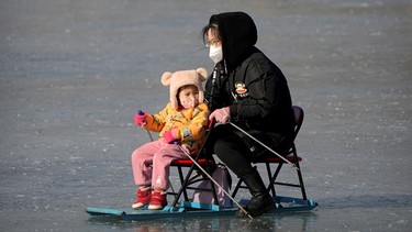 Eine Frau fährt 2023 mit einem Kind, auf einem zugefrorenen Teich in einem öffentlichen Park in Peking. Chinas Bevölkerung ist im vergangenen Jahr erstmals seit sechs Jahrzehnten geschrumpft.  | Bild: dpa-Bildfunk/Mark Schiefelbein