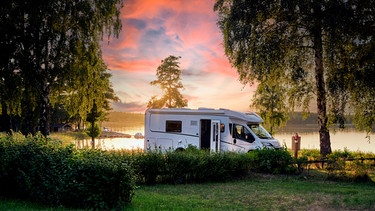 Ein Wohnmobil steht während des Sonnenuntergangs an einem See in Schweden. | Bild: stock.adobe.com/www.push2hit.de