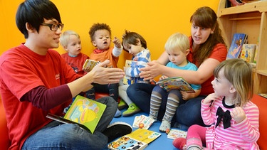 Kinder schauen gemeinsam mit Erziehern Bilderbücher an. | Bild: picture-alliance/dpa