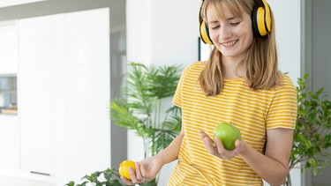 Happy woman wearing wireless headphones holding green apple and lemon | Bild: picture alliance / Westend61 | Svetlana Karner