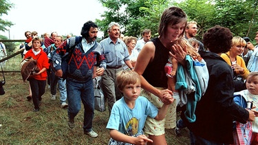 DDR-Flüchtlinge mit ihren Kindern gehen durch das geöffnete Grenztor von Ungarn aus nach Österreich (Archivbild vom 19.08.1989). | Bild: picture-alliance/dpa