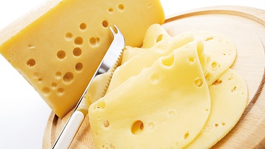 Symbolbild: Ein Stück Käse neben Käsescheiben auf einem Holzbrett | Bild: MEV/Creativstudio