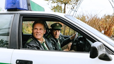 Hubert und Staller im Streifenwagen sitzend. | Bild: BR