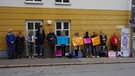 Menschen mit Plakaten stehen vor einer gelben Wand | Bild: Bayerischer Rundfunk 2024