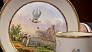 "Ballon"-Tasse. Vielleicht ist es das Ehepaar Reichard, deutsche Luftfahrtpioniere, die auf dieser Meissener Tasse mit Untertasse aus dem Jahr 1811 dargestellt sind. Und welche Szene ist im Hintergrund zu sehen? Geschätzter Wert: 2.000 Euro | Bild: Bayerischer Rundfunk