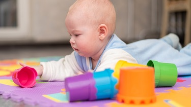 Ein Baby spielt am Boden mit Stapelbechern. | Bild: colourbox.com