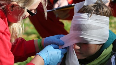 Ein Mädchen legt einem Jungen einen Kopfverband an. | Bild: picture-alliance/dpa
