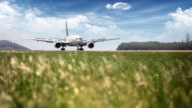 Ein startendes Flugzeug auf dem Rollfeld. Im Vordergrund ist grüne Wiese. | Bild: colourbox.com