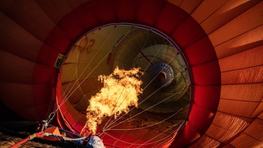 Ein Heißluftballon kurz vor dem Start (von unten aufgenommen): Man sieht den Brenner, der die Luft erwärmt. | Bild: picture alliance / ZUMAPRESS.com | Marco Alpozzi