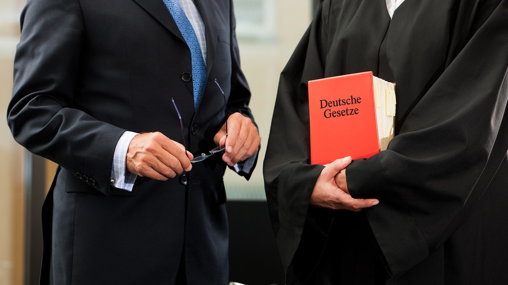 Eine Richterin hält das Deutsche Gesetzbuch in den Armen, während sie sich mit einem Mann im dunklen Anzug unterhält. | Bild: colourbox.com