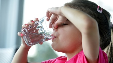 Ein Mädchen trinkt ein Glas Wasser und hält dabei die Luft an um ihren Schluckauf loszuwerden. | Bild: picture-alliance/dpa | Frank May