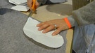Aus dem grauen Wollstoff werden mit einer Schere die Teile für einen Mantel ausgeschnitten. | Bild: BR | Kathrin Reikowski