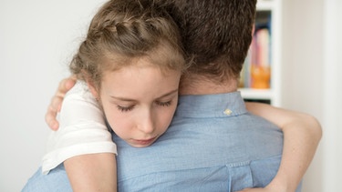 Ein traurig wirkendes Kind umarmt seinen Vater. | Bild: colourbox.com