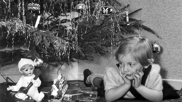 Weihnachten 1955: Ein Kind liegt unter einem lamettageschmückten Christbaum. | Bild: picture-alliance/dpa