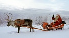 Der Weihnachtsmann auf seinem von einem Rentier gezogenen Schlitten im Schnee. | Bild: picture-alliance/dpa