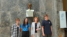 MünchenHören 2021: Drei Schülerinnen und Schüler mit Dr. Hildegard Kronawitter vor der Marmorbüste von Sophie Scholl in der LMU.  | Bild: BR | Judith Schönicke