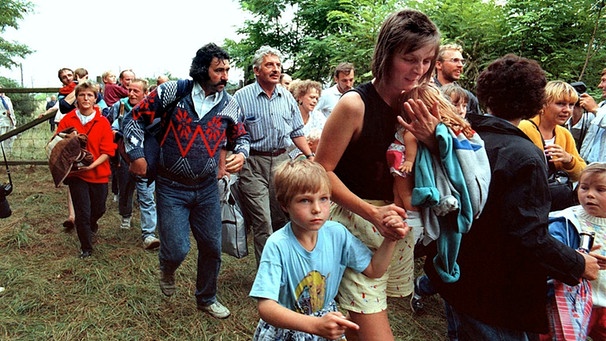 DDR-Flüchtlinge mit ihren Kindern gehen durch das geöffnete Grenztor (Archivbild vom 19. August 1989). Etwa 600 DDR-Bürger nutzten ein paneuropäisches Picknick an der ungarisch-österreichischen Grenze, bei dem ein Grenztor symbolisch geöffnet wurde, zur Flucht in den Westen. | Bild: picture-alliance/dpa