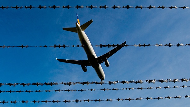 Symbolbild Abschiebung: Ein Stacheldraht von unten fotografiert, darüber fliegt eine Flugzeug | Bild: picture-alliance/dpa
