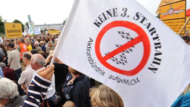 Demonstrant winkt am Flughafen München mit einer Fahne des Aktionsbündnisses "AufgeMUCkt" gegend en Bau einer dritten Startbahn (Archiv) | Bild: picture-alliance/dpa