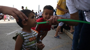 Flüchtlingslager im stillgelegten Flughafen Athen-Ellinikon: Kind trinkt aus einem Schlauch Wasser | Bild: picture-alliance/dpa