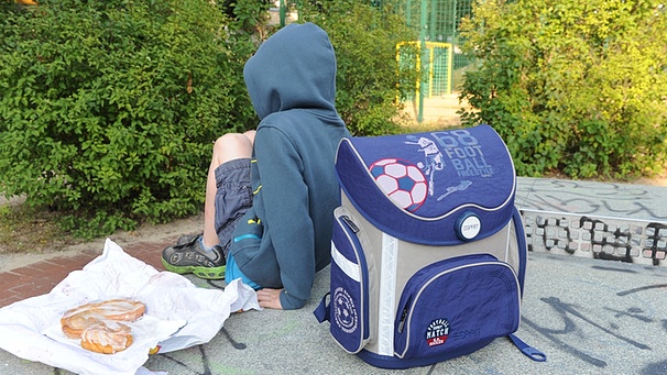 Ein Bub sitzt mit seinem Schulranzen auf einer Tischtennisplatte auf einem Spielplatz | Bild: picture-alliance/dpa