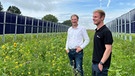 Franz Obermayer Junior und Senior stehen zwischen zwei Reihen mit vertikalen Photovoltaikmodulen. | Bild: BR / Lisa Westhäußer